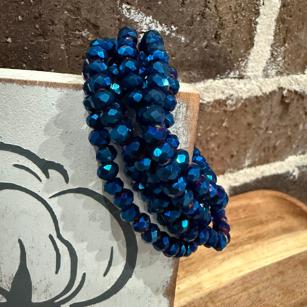 Blue beaded bracelet on a wooden block with a stone wall background