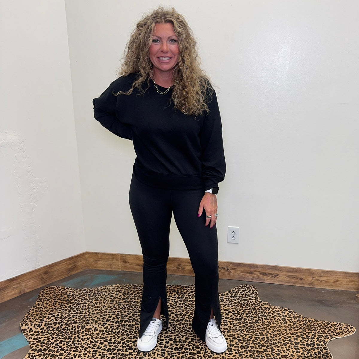  black outfit standing on a leopard print rug in a room with white walls and wooden floor.