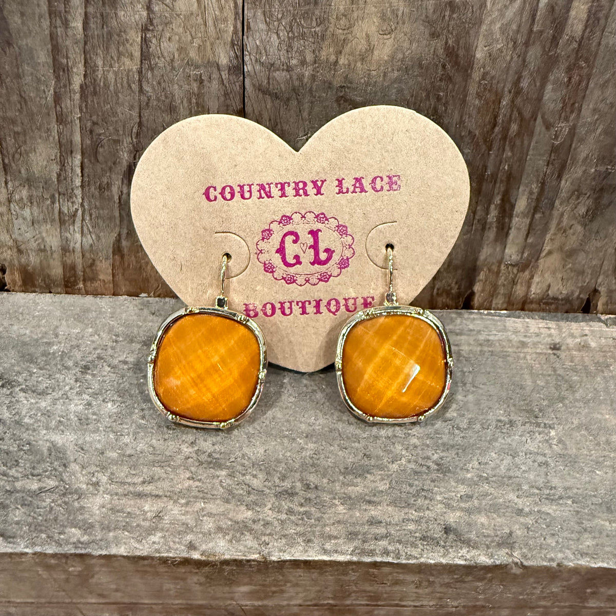 Pair of earrings on a heart-shaped card with 'Country Lace Boutique' branding, placed on a wooden surface.