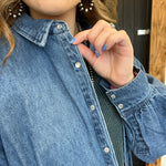 Person wearing a blue denim jacket with a close-up of the collar and buttons.