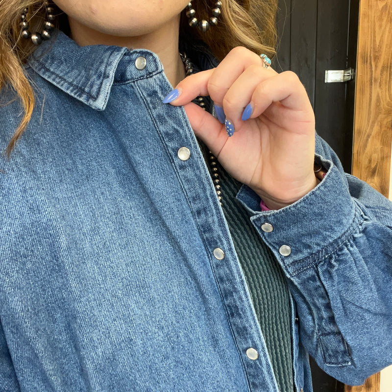 Person wearing a blue denim jacket with a close-up of the collar and buttons.