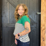 Woman wearing a green and black striped shirt standing in front of a wooden door.
