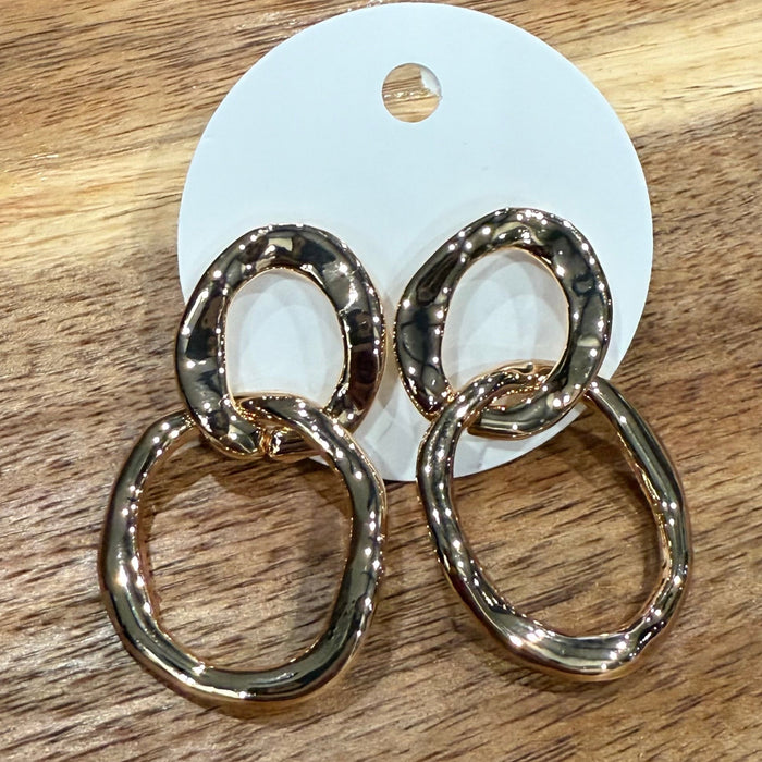 Gold hoop earrings on a white card, placed on a wooden surface