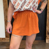 Person wearing an orange skirt and a white crop top with text, standing indoors.
