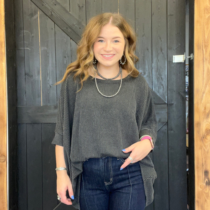 Woman wearing a gray sweater and blue jeans standing in front of a wooden door.