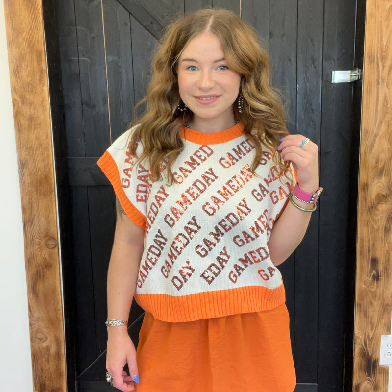 Person wearing a 'GAMEDAY' sweater with orange and white colors, standing in front of a wooden door.