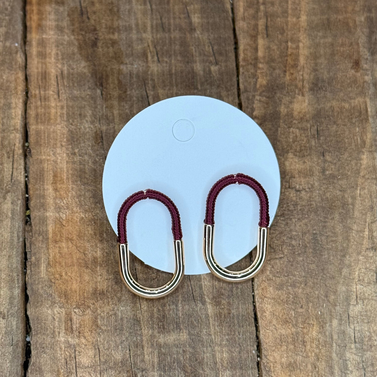 Carabiner-shaped earrings with red loops on a light blue card against a wooden background