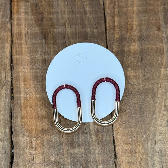 Carabiner-shaped earrings with red loops on a light blue card against a wooden background