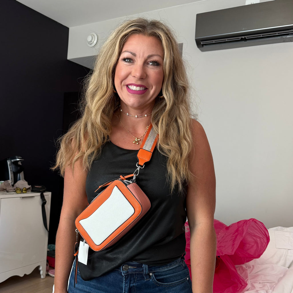 Woman holding a crossbody bag with a visible brand tag in a room.