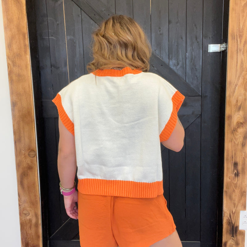 Person wearing an orange and white sleeveless top and shorts standing in front of a wooden door.
