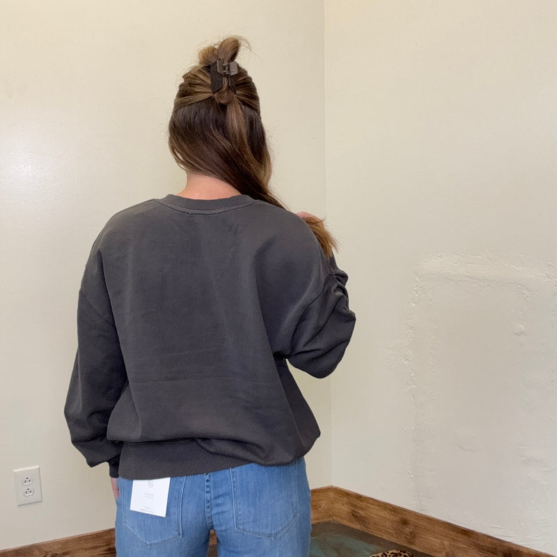 Person wearing a dark gray sweatshirt and blue jeans standing against a plain wall.