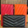 Three quilted leather wallets in red, black, and orange on a wooden surface.