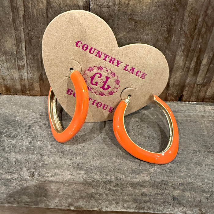 Orange hoop earrings on a heart-shaped 'Country Lace Boutique' card against a wooden background.
