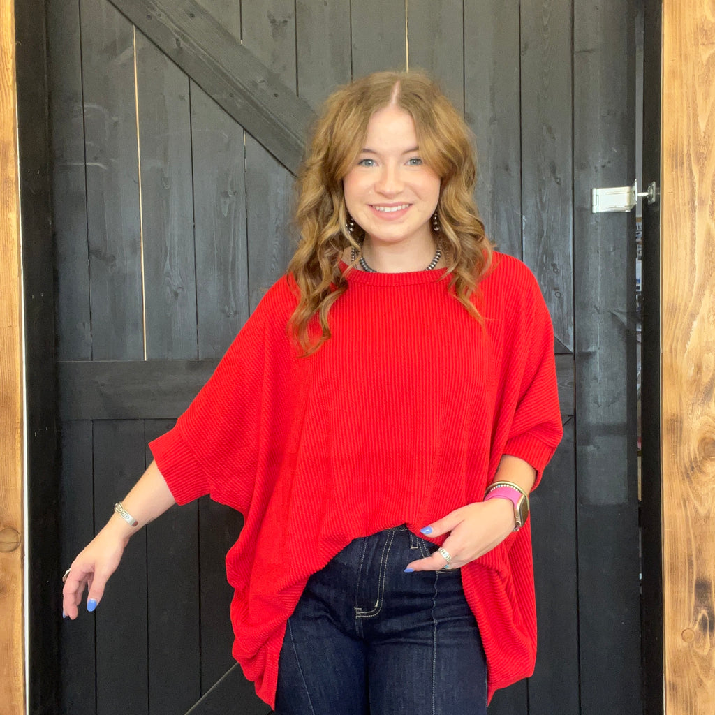 Woman wearing a red sweater standing in front of a wooden door.