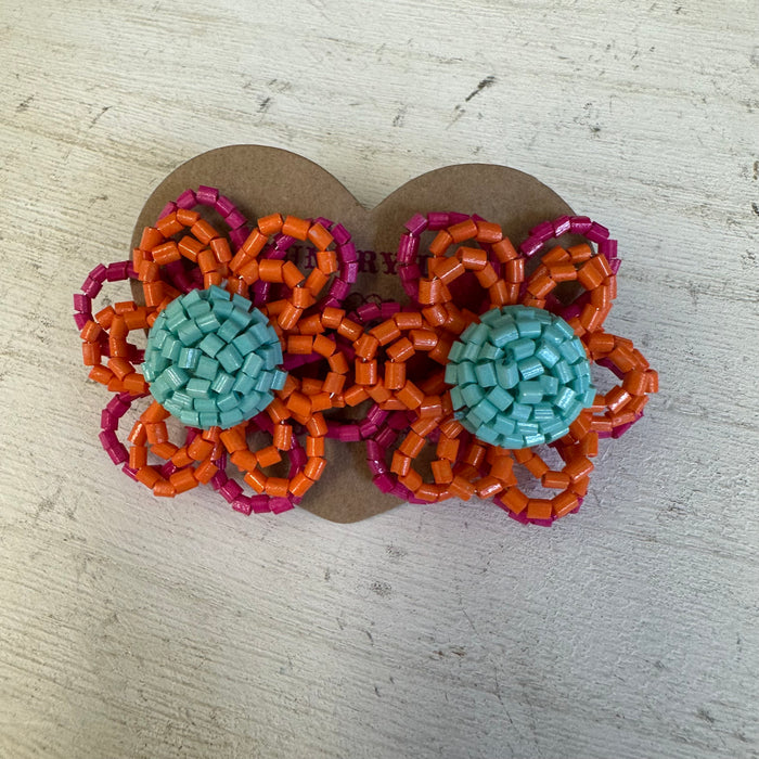 Pair of earrings with orange, pink, and teal beads on a light wooden surface