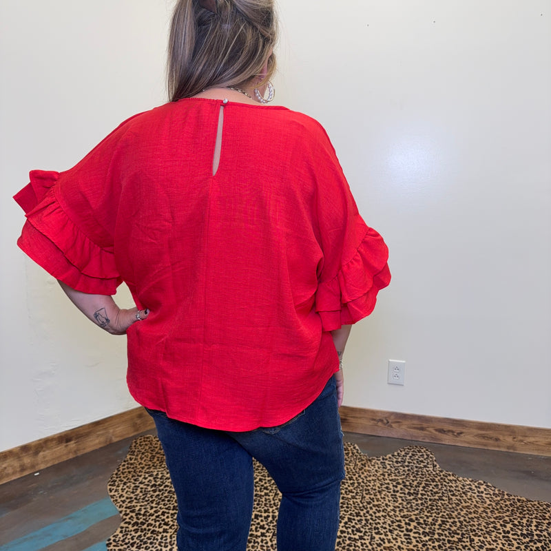 red blouse with ruffled sleeves in a room with a white wall and wooden floor.