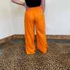 Person wearing bright orange pants standing on a leopard print rug.