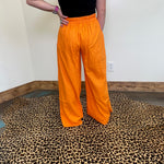 Person wearing bright orange pants standing on a leopard print rug.
