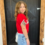 Person wearing a red sleeveless jacket with 'Gildan' branding, standing in front of a wooden door.