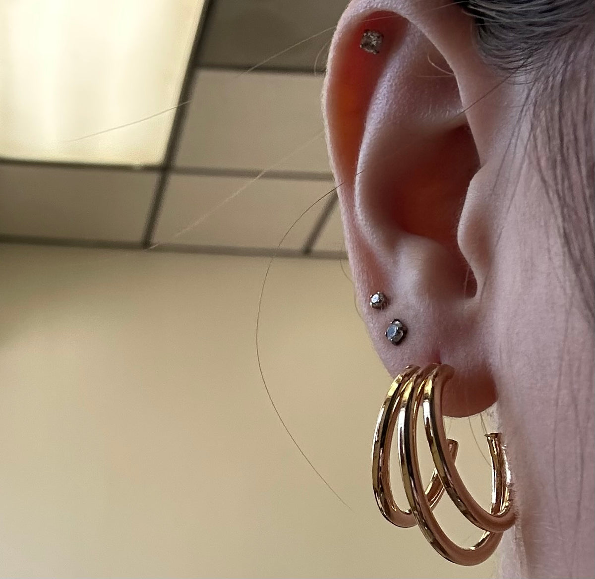 Close-up of an ear with gold hoop earrings and multiple piercings.
