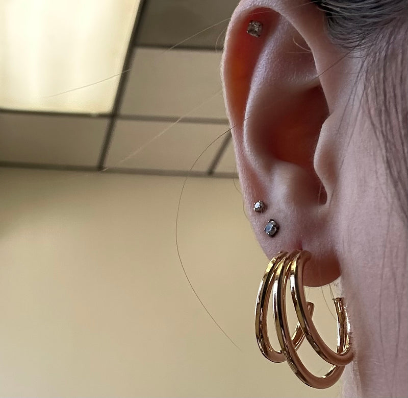 Close-up of an ear with gold hoop earrings and multiple piercings.