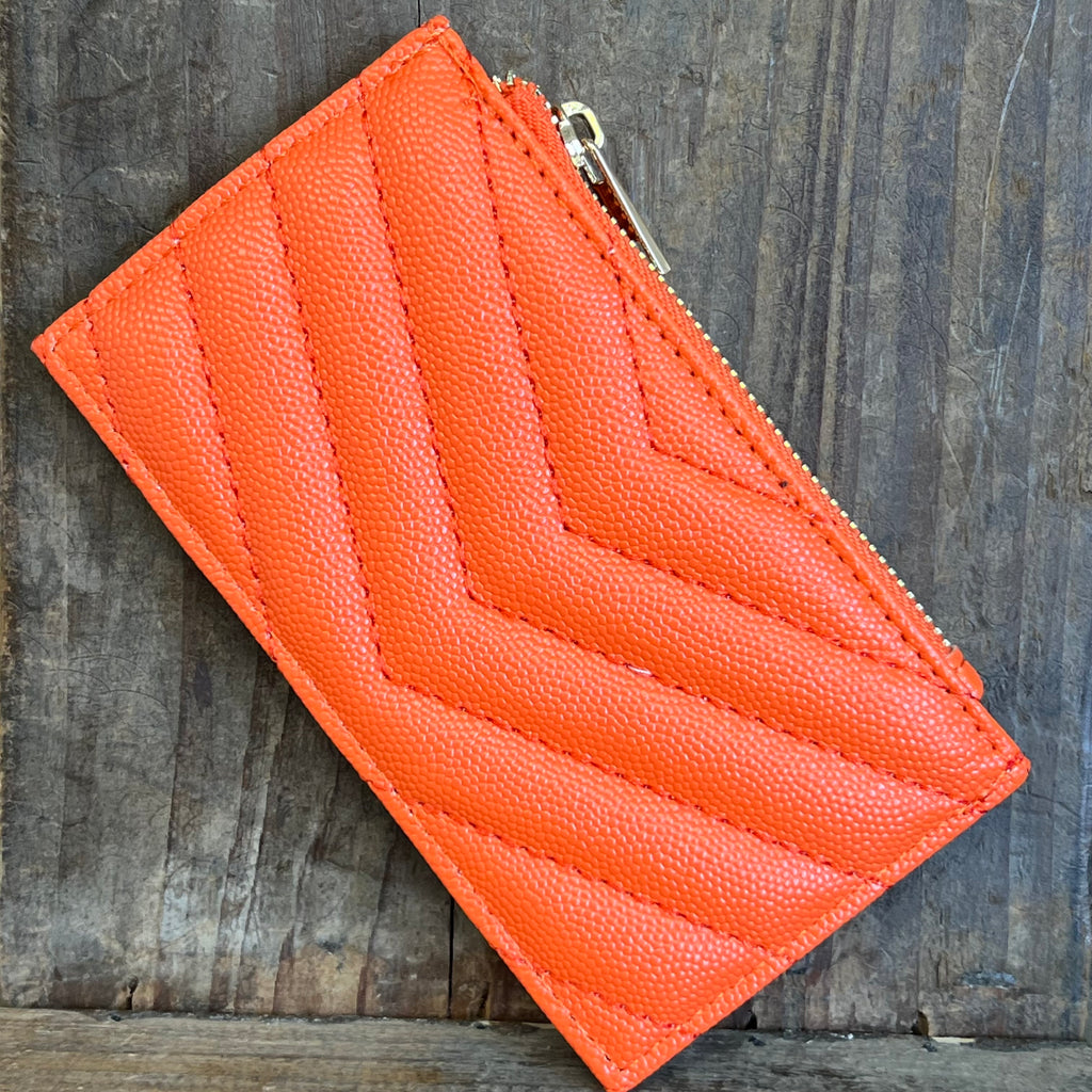 Orange quilted wallet with a zipper on a wooden surface