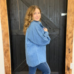Woman wearing a blue denim jacket standing in front of a wooden door.
