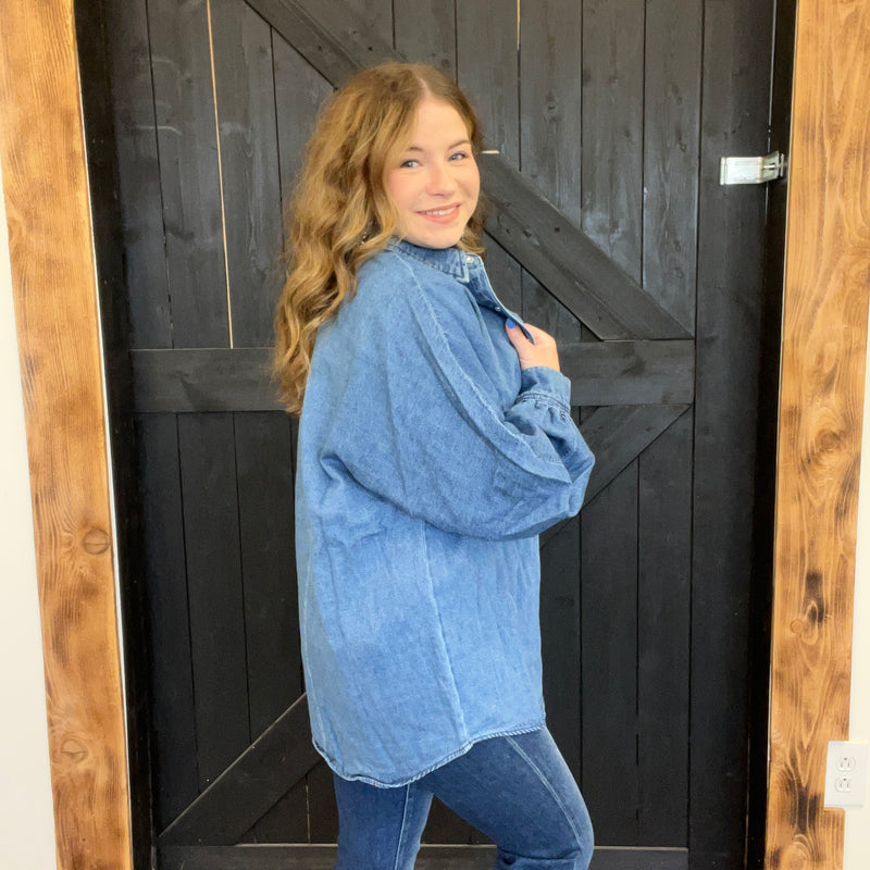 Woman wearing a blue denim jacket standing in front of a wooden door.