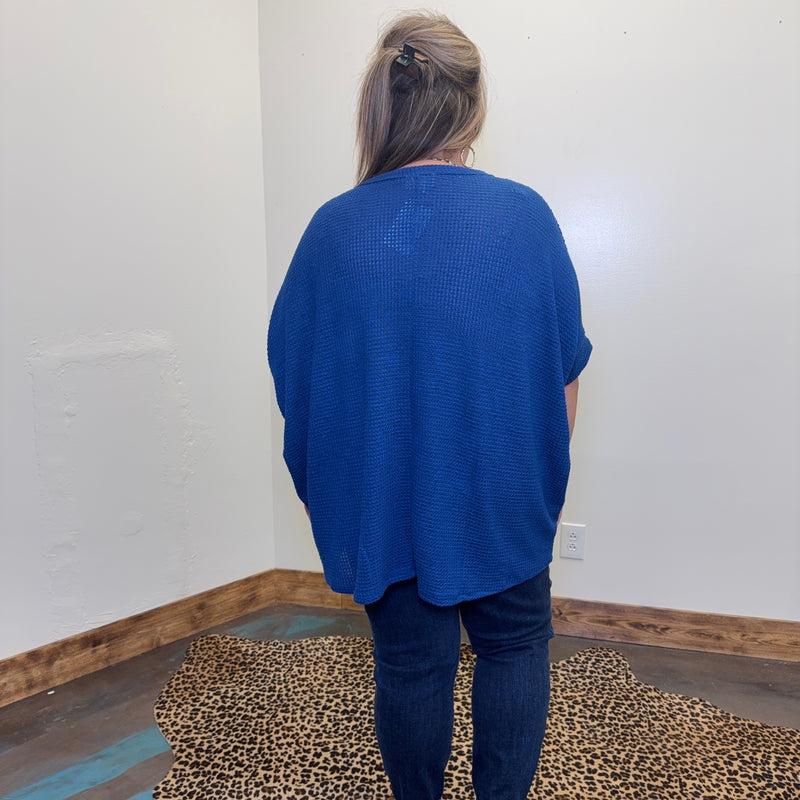 Person wearing a blue shirt and dark pants standing in a room with a leopard print rug.