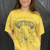 Person wearing a yellow t-shirt with a cowboy graphic design against a wooden background