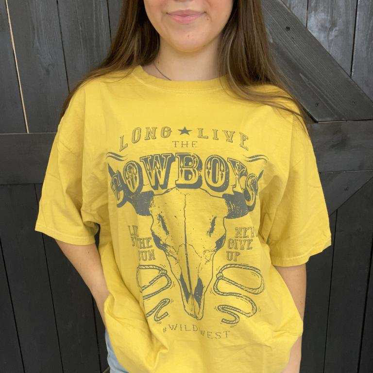 Person wearing a yellow t-shirt with a cowboy graphic design against a wooden background