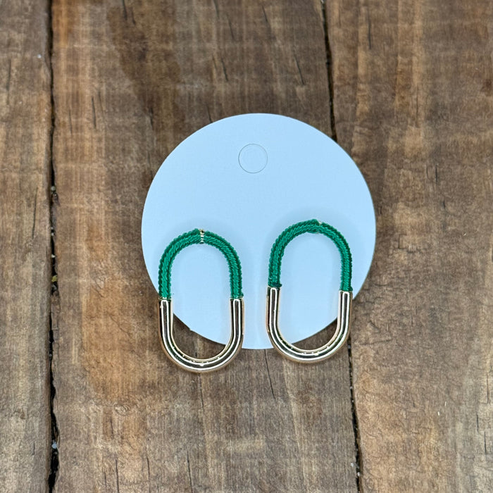 Green and silver earrings on a blue card against a wooden background