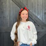 Person wearing a white sweatshirt with a logo and text, standing against a wooden background