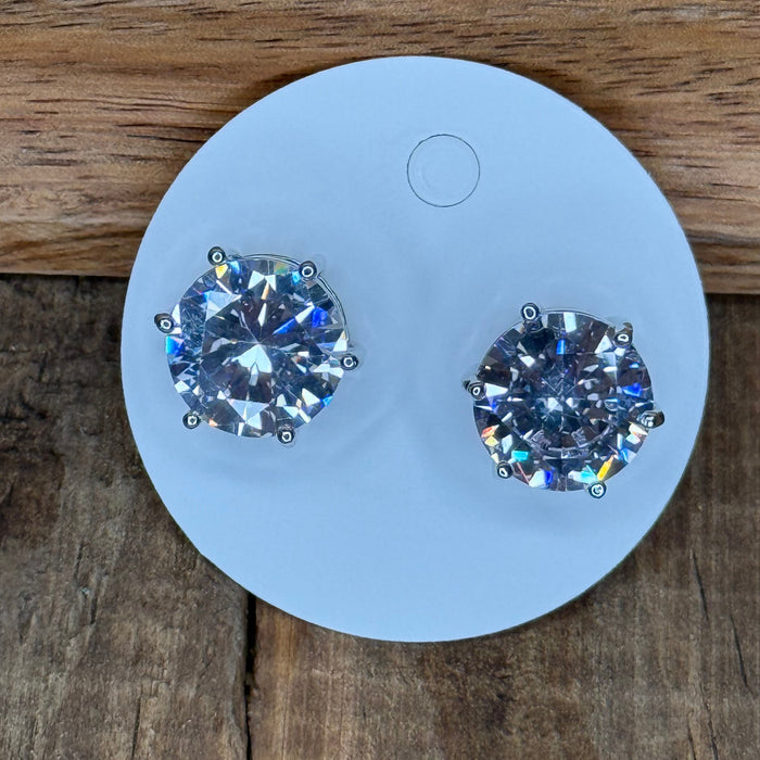 Two diamond earrings on a white round stand against a wooden background