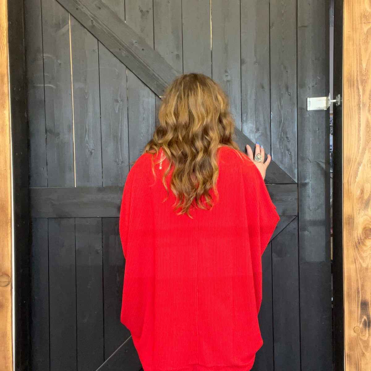 Person wearing a red sweater standing in front of a wooden door.