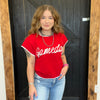 Person wearing a red 'Gameday' shirt standing in front of a wooden door.
