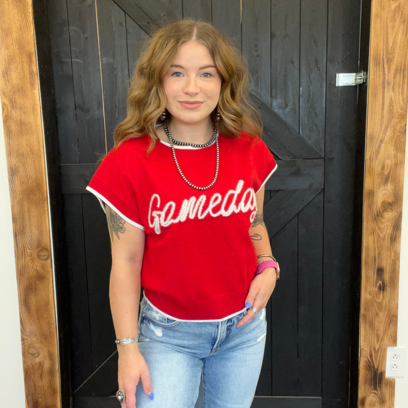 Person wearing a red 'Gameday' shirt standing in front of a wooden door.