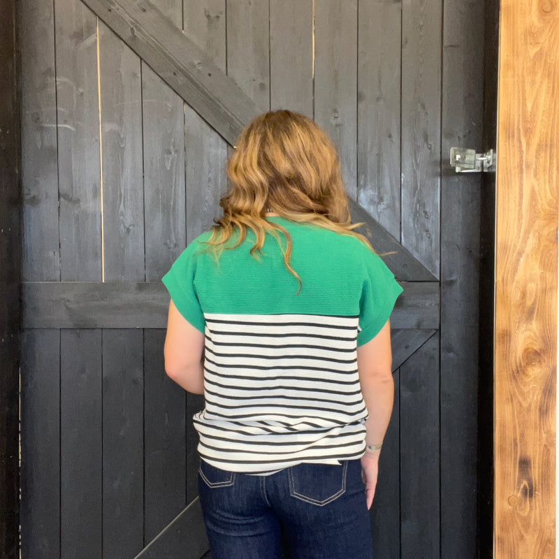 Person wearing a green and white striped shirt standing in front of a wooden door.