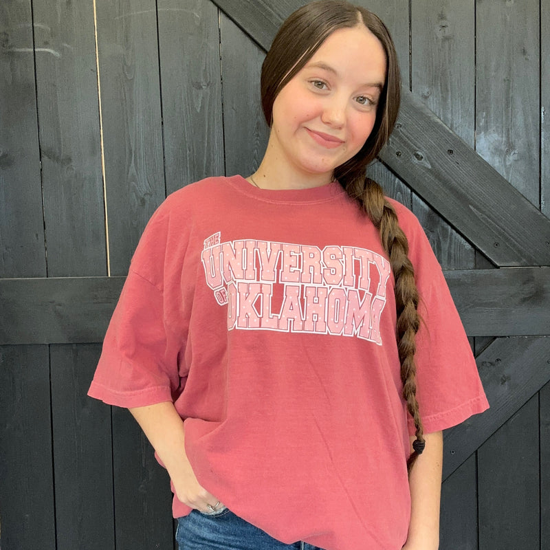 Person wearing a red 'University of Oklahoma' t-shirt against a wooden background