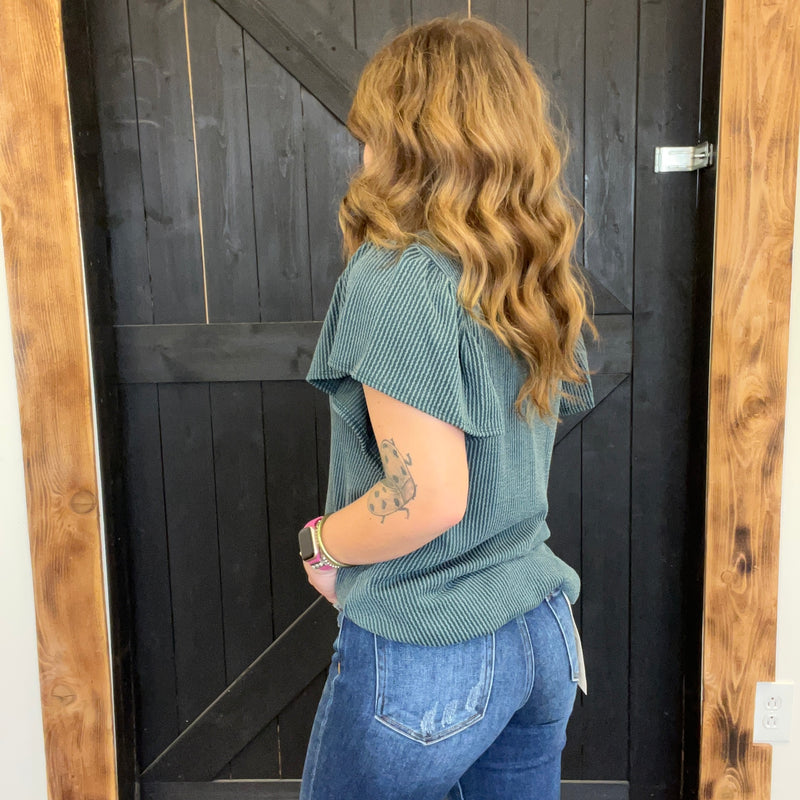 Person wearing a green shirt and blue jeans standing in front of a wooden door.
