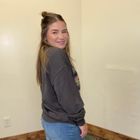 Person wearing a dark gray sweatshirt and blue jeans standing against a plain wall.