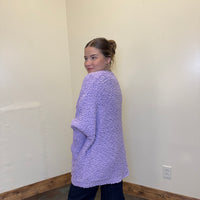 Person wearing a purple textured sweater standing against a plain wall.