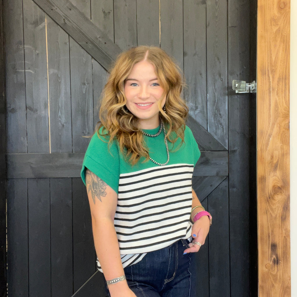 Woman wearing a green and black striped shirt standing in front of a wooden door.
