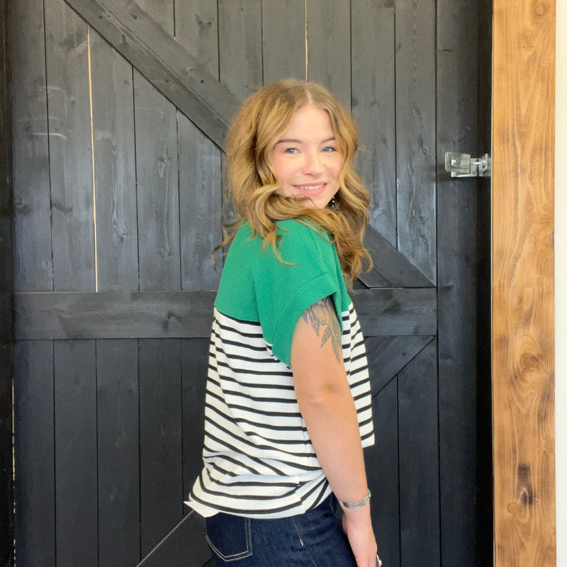 Woman wearing a green and black and white striped shirt standing in front of a wooden door.