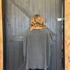 Person wearing a gray sweater standing in front of a wooden door.