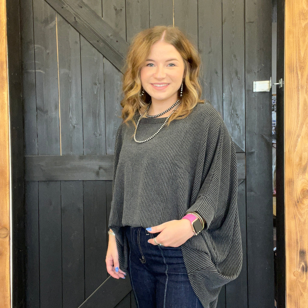 Woman wearing a gray sweater and dark jeans standing in front of a wooden door.