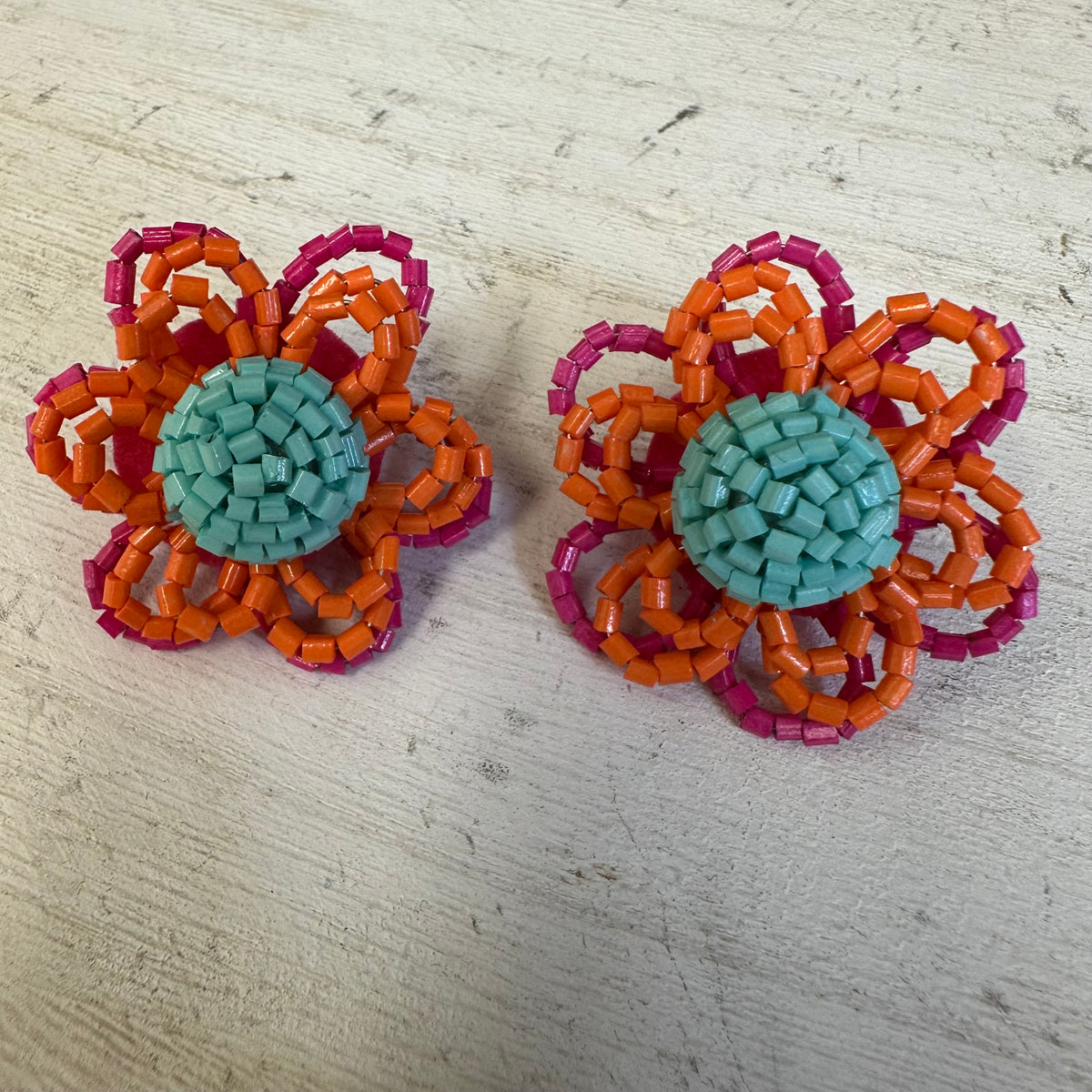 Pair of flower-shaped earrings with orange, pink, and teal colors on a light wooden surface.