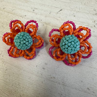 Pair of flower-shaped earrings with orange, pink, and teal colors on a light wooden surface.