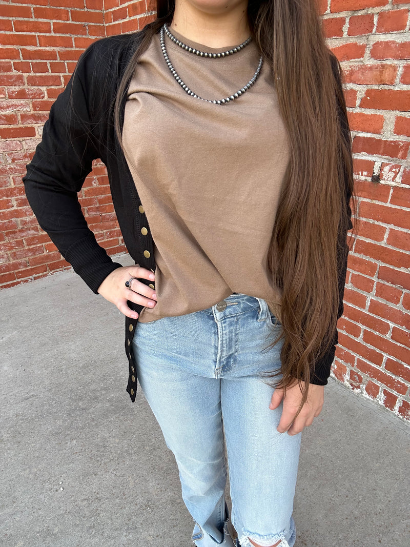 Person wearing a beige jacket and light blue jeans on a brick pavement.