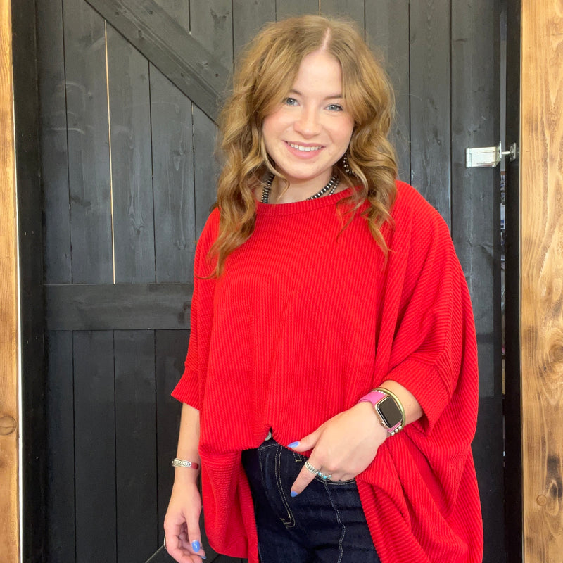 Woman wearing a red sweater standing in front of a wooden door.